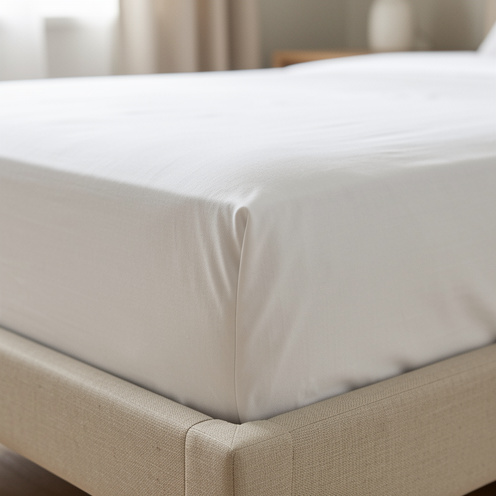Drap-housse blanc en coton bien ajusté sur un matelas une place, avec un gros plan sur son bonnet élastiqué et la texture du tissu.
