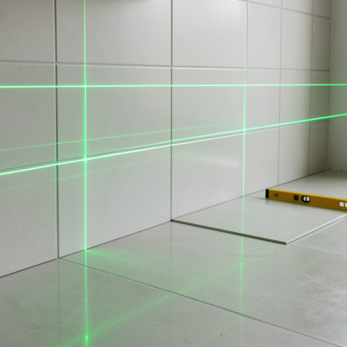 Niveau laser projetant des lignes vertes horizontales et verticales pour aligner précisément des carreaux dans un intérieur en rénovation.