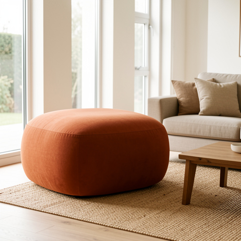 Grand pouf d’intérieur en tissu terracotta installé dans un salon contemporain chaleureux, avec une table basse en bois et un tapis tissé.